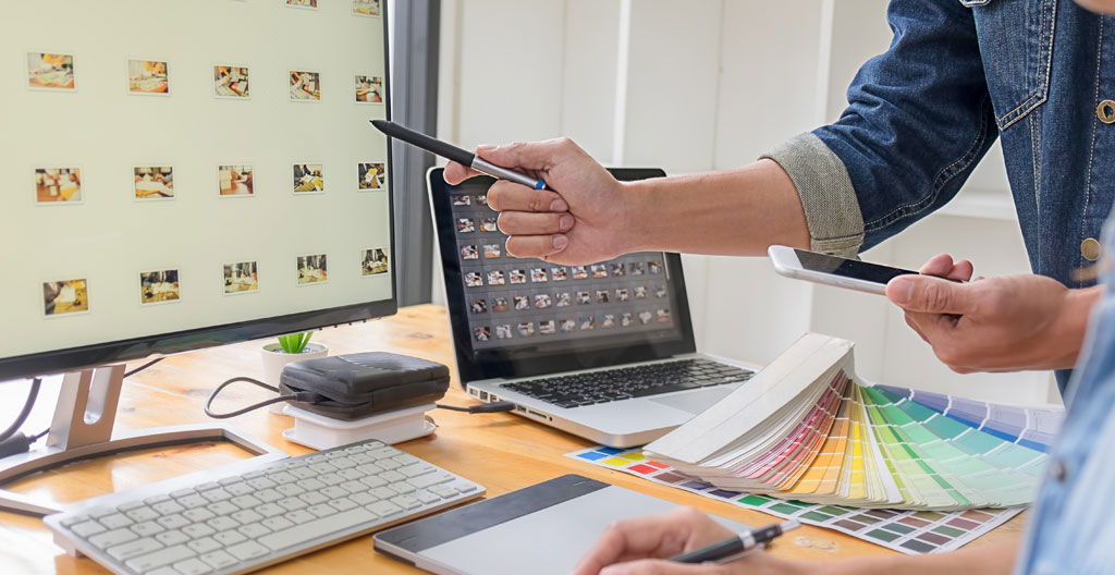 Bureau de consultant avec portfolio de réalisations graphiques variées disposées professionnellement : cartes de visite, brochures, affiches, tablette montrant site web, smartphone avec motion design, photos d'enseignes, démontrant amplitude des supports possibles